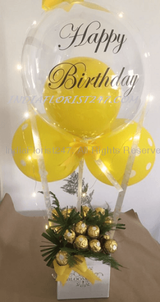 Yellow Balloon inside a transparent Balloon with text Happy Birthday 2 yellow balloons outside tied to a box of 16 Ferrero Rocher chocolates and roses adorned with yellow ribbons and led lights C-BFST